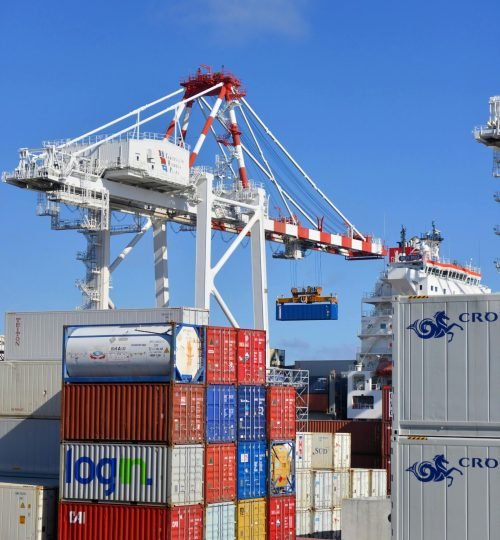 Colorful shipping containers stacked in a busy port with cranes overhead.